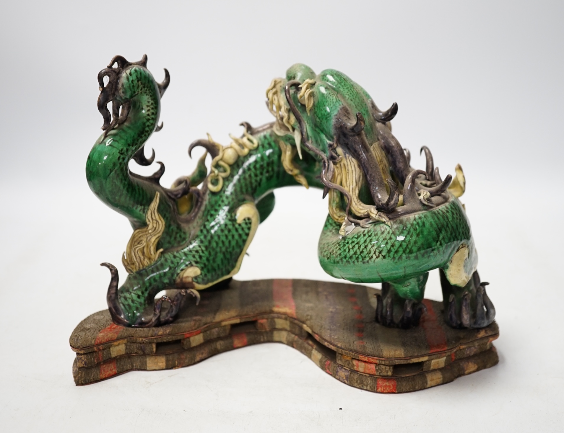A Chinese sancai glazed model of a dragon, silk covered stand, 28cm wide. Condition - some damage